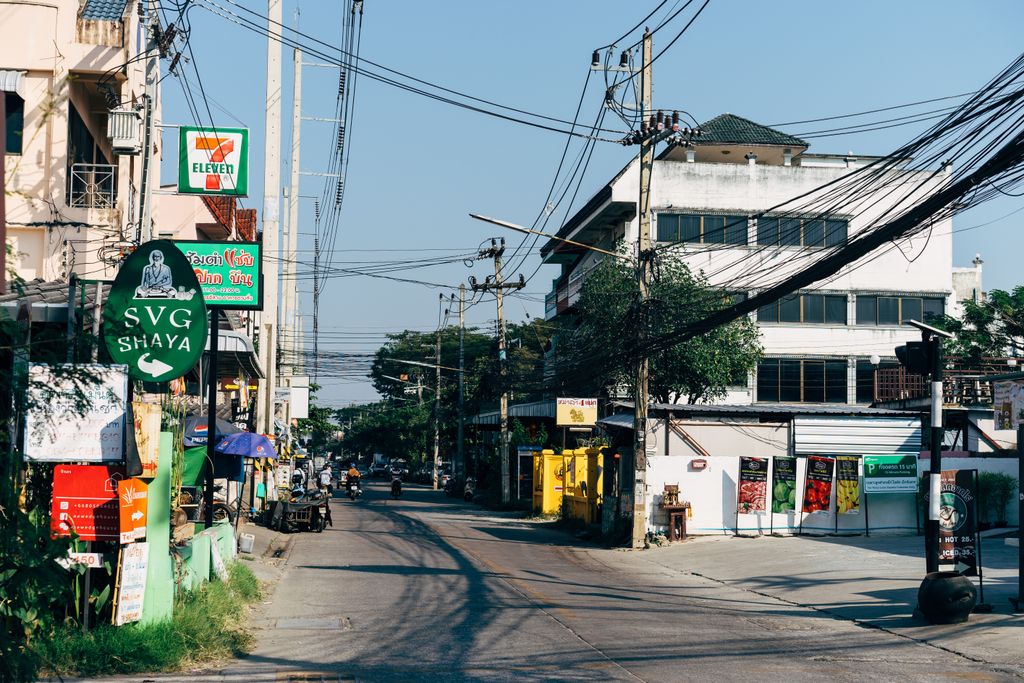 A bustling urban street in Chiang Mai, Thailand showcasing shops, power lines, and signages.