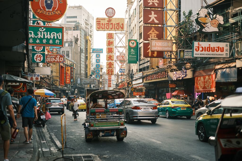 Bustling street scene in Bangkok's Chinatown with colorful signs and tuk-tuks.